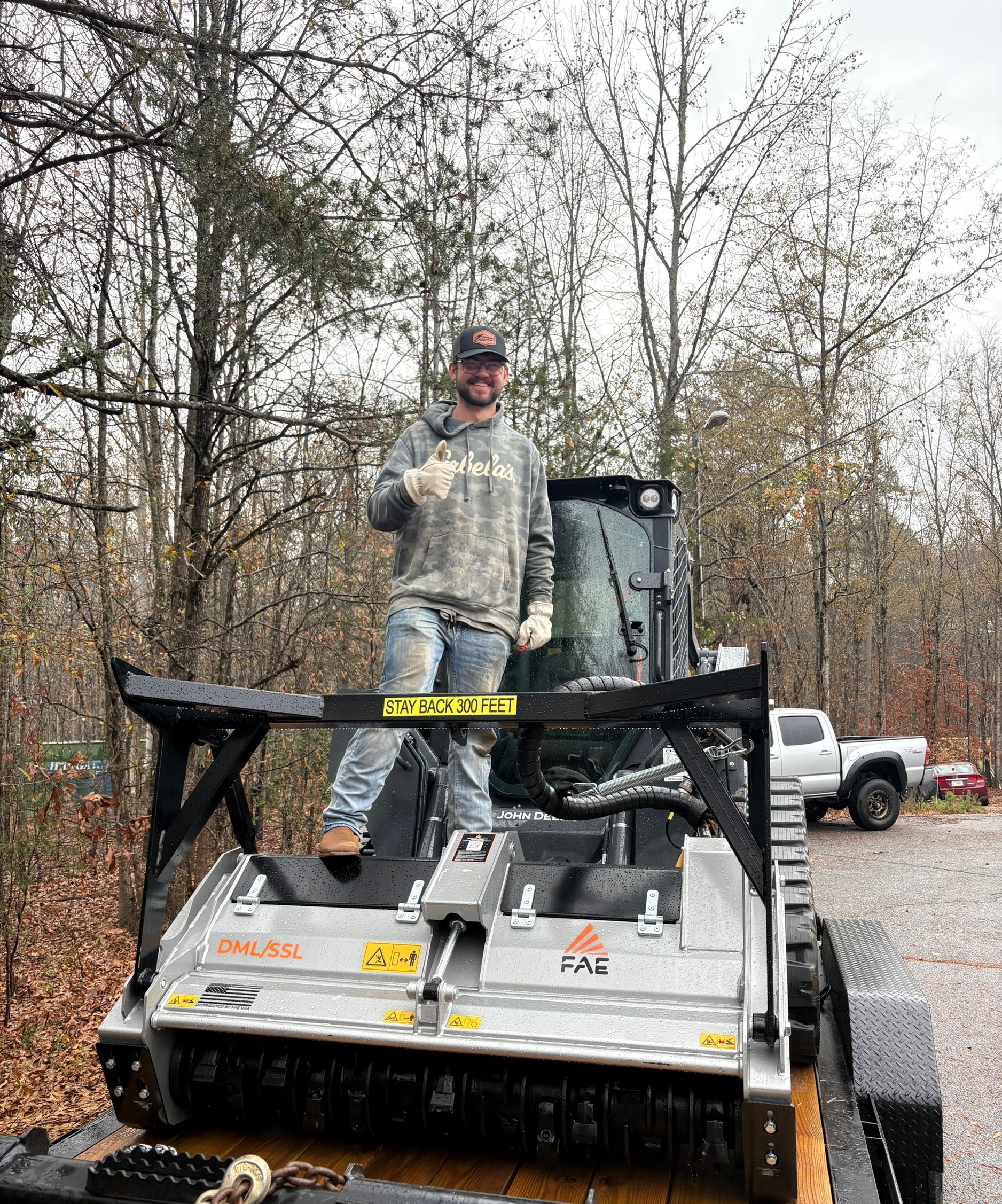 Jayton Fisher owner of Fisher's Forestry and Land Management standing on John Deere 325G with FAE forestry mulcher in Greenville SC